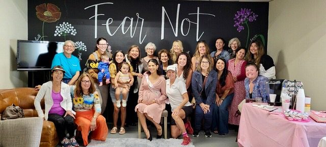 A room full of women gathered for a baby shower in front of a wall that reads Fear Not